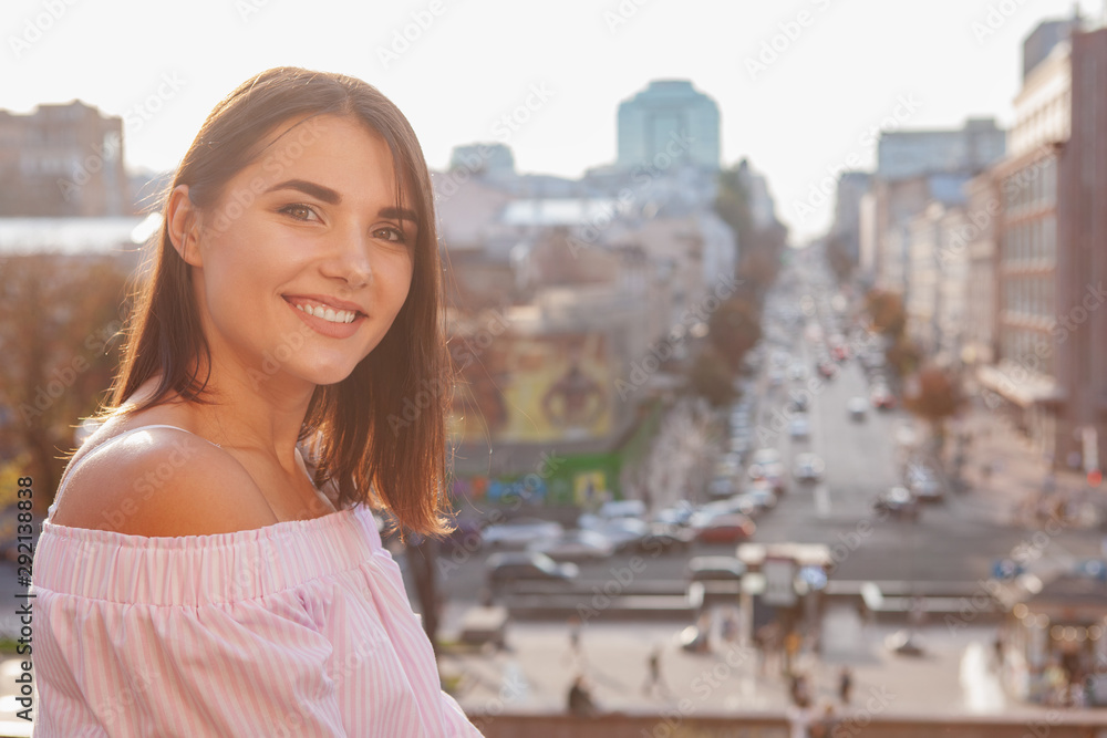 Close up of a happy beautiful woman smiling to the camera, enjoying wandering in the city on a warm autumn day, copy space