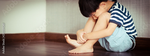 A difficult little Asian boy sits and left alone in room, hugs knees up and face down staring at his toe. Childhood mental health, Unsociable, Introvert kids, Autism, Emotional abuse effects. Banner. photo