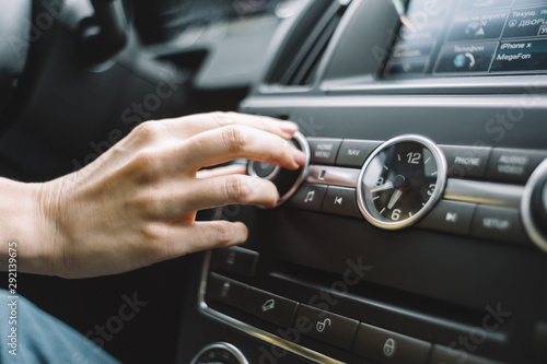 Close up photo of a female finger that reaches out to turn up volume on the multimedia system. Selective focus. Listening music in the auto. Car clock. Interior of automobile. Travelling by car.  © Denis Mamin