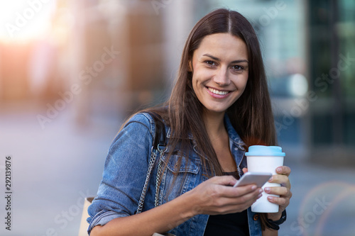 Young woman with smartphone and coffee in the city 