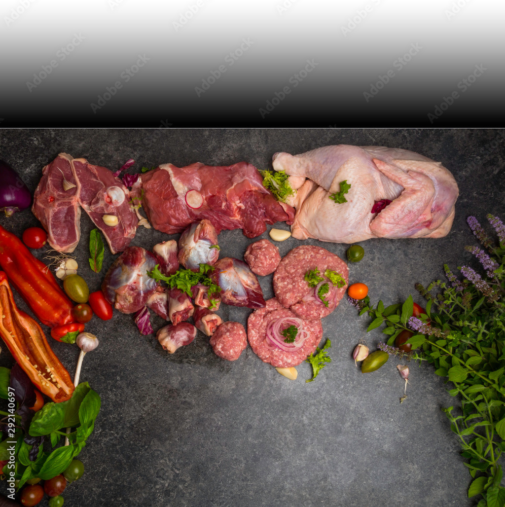 Assorted raw meat on dark background with cherry tomatoes, mint leaves, greenery, garlic, different types of meat and processed food. Top view, vintage toned image, blank space