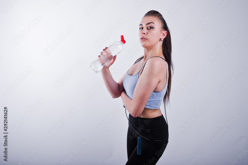 Cheerful attractive young fitness woman in top and black leggings with jump rope and bottle of water isolated over white background. Cheerful attractive young fitness woman in top and black leggings with jump rope and bottle of water isolated over white background.
