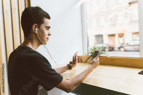 Young adult text message on smartphone and listen to music on headphones in cafe. Lifestyle, free time, rest, relaxation