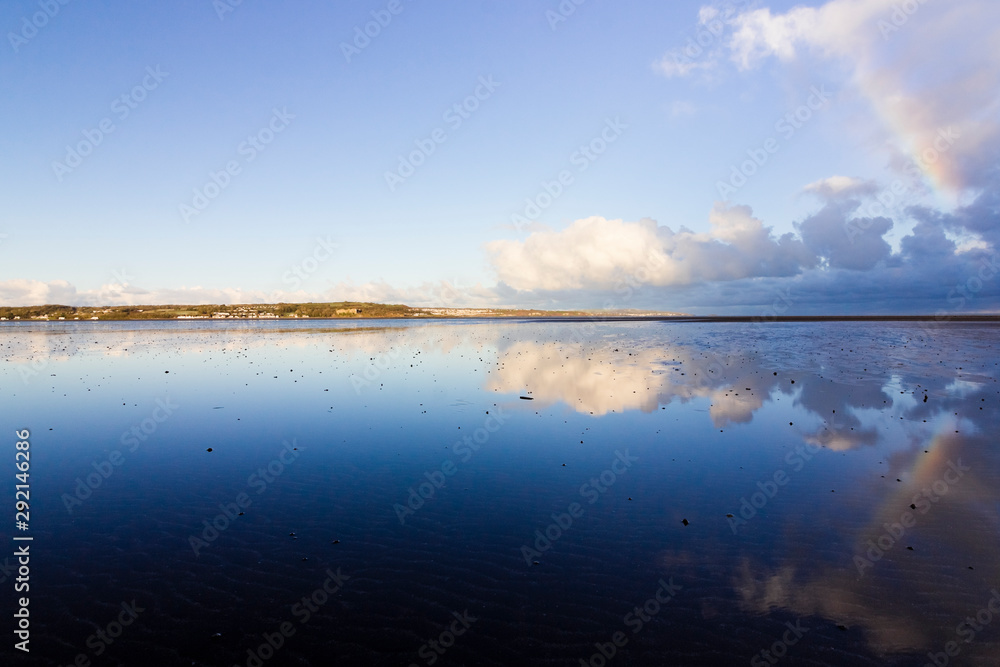 Beautiful coastal vista from Red Wharf Bay including a passing rain shower and partial rainbow reflecting on the surface of the bay, Isle of Anglesey, North Wales