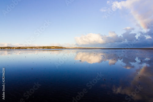 Beautiful coastal vista from Red Wharf Bay including a passing rain shower and partial rainbow reflecting on the surface of the bay, Isle of Anglesey, North Wales