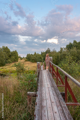 A girl is standing on a suspension bridge across a forest river © Andrey Nikitin