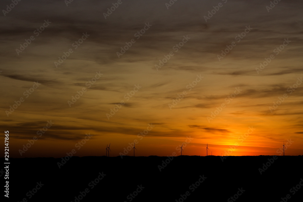 Beautiful Sunset with a glowing cloudy sky with wind turbines on on the hills on the horizon