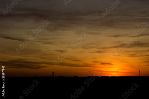 Beautiful Sunset with a glowing cloudy sky with wind turbines on on the hills on the horizon