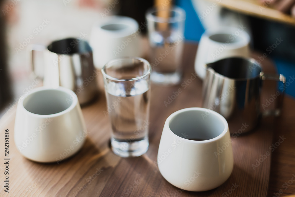 White cups of black coffee, steel coffee pots, glasses of water, wooden table White cups of black coffee, steel coffee pots, glasses of water, wooden table