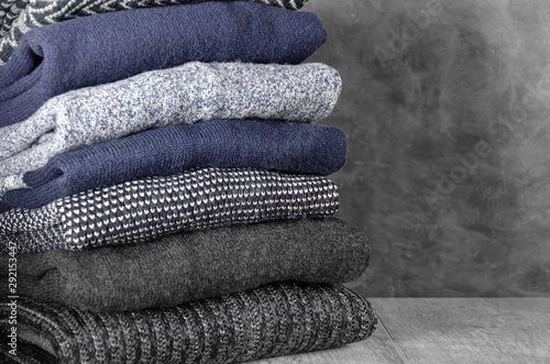 Stack of folded warm knitted men's sweaters on gray background. Closeup. Copy space
