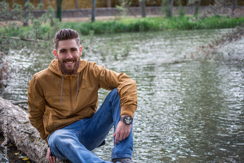 Handsome smiling man sitting on the trunk of a tree floating in the river. Copyspace right.