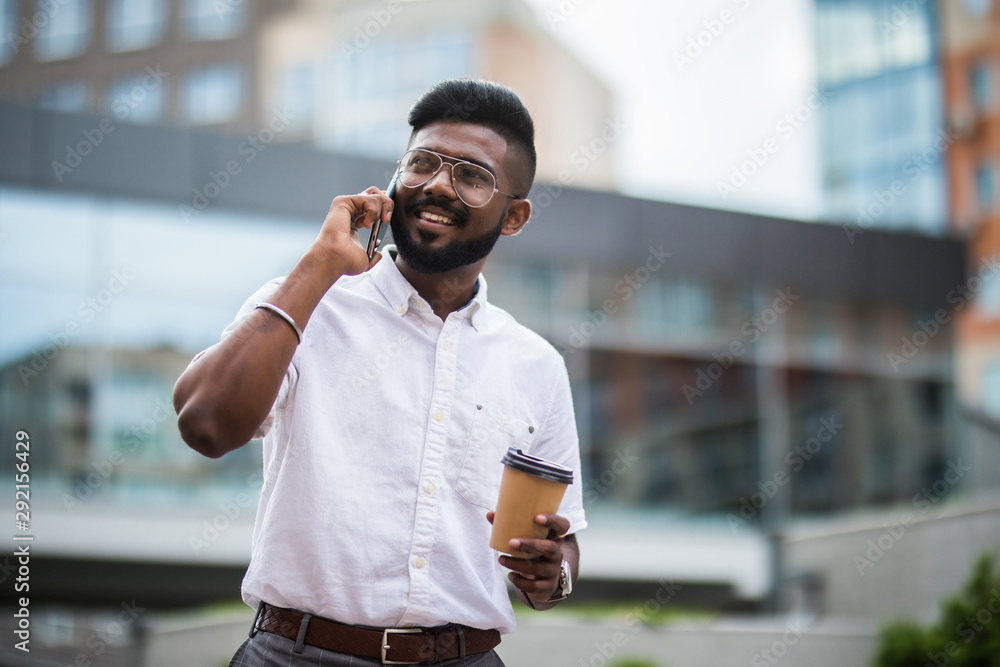 Indian man talking on mobile phone and drinking coffee - obrazy, fototapety, plakaty 
