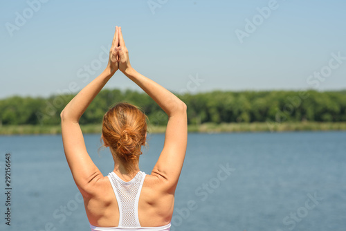Young girl practices yoga near the river on a clear sunny day