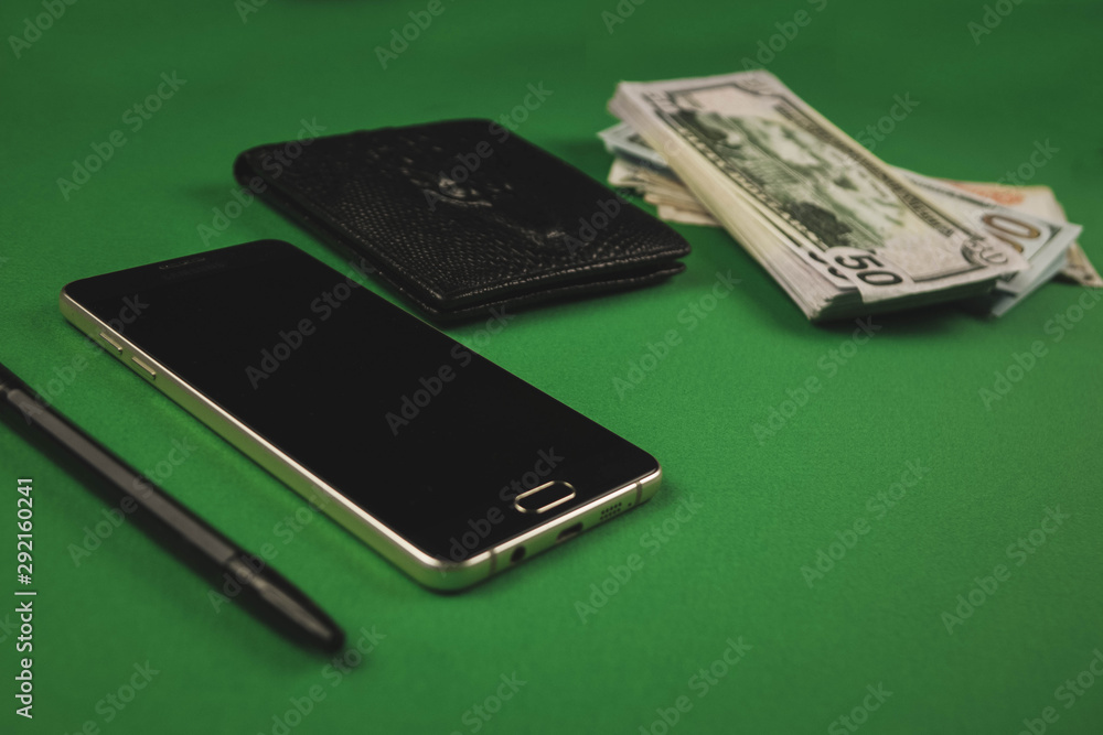 Φωτογραφία a lot of cash packs, telephone, black pen and wallet lying on a green background