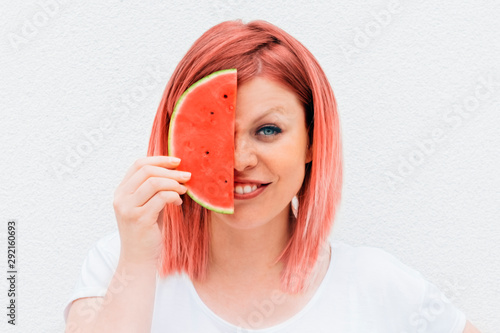 beautiful smiling redhead woman holding a slice of watermelon against a white wall as background. Healthy lifestyle concept
