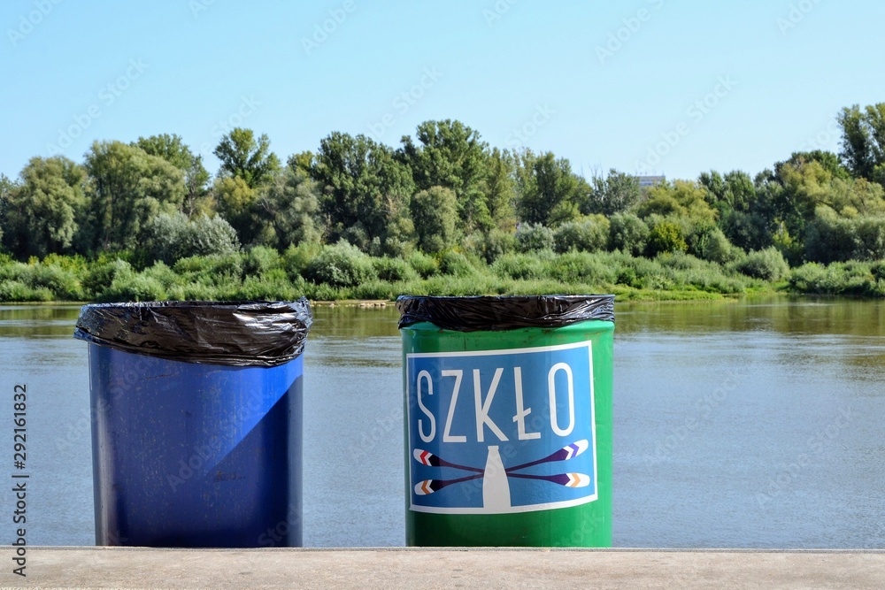 Trash bin placed on the river bank. Inscription on the bin glass