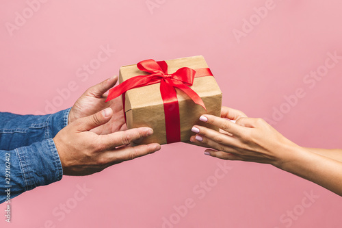 Top view of male and female hands holding red gift box with golden ribbon on pink background Flat lay. Present for birthday, valentine day, Christmas, New Year. Congratulations background copy space. photo