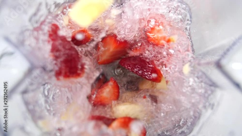 Banana and strawberry smoothie juice poured into a blender using fruit and water against a white background with macro shot.