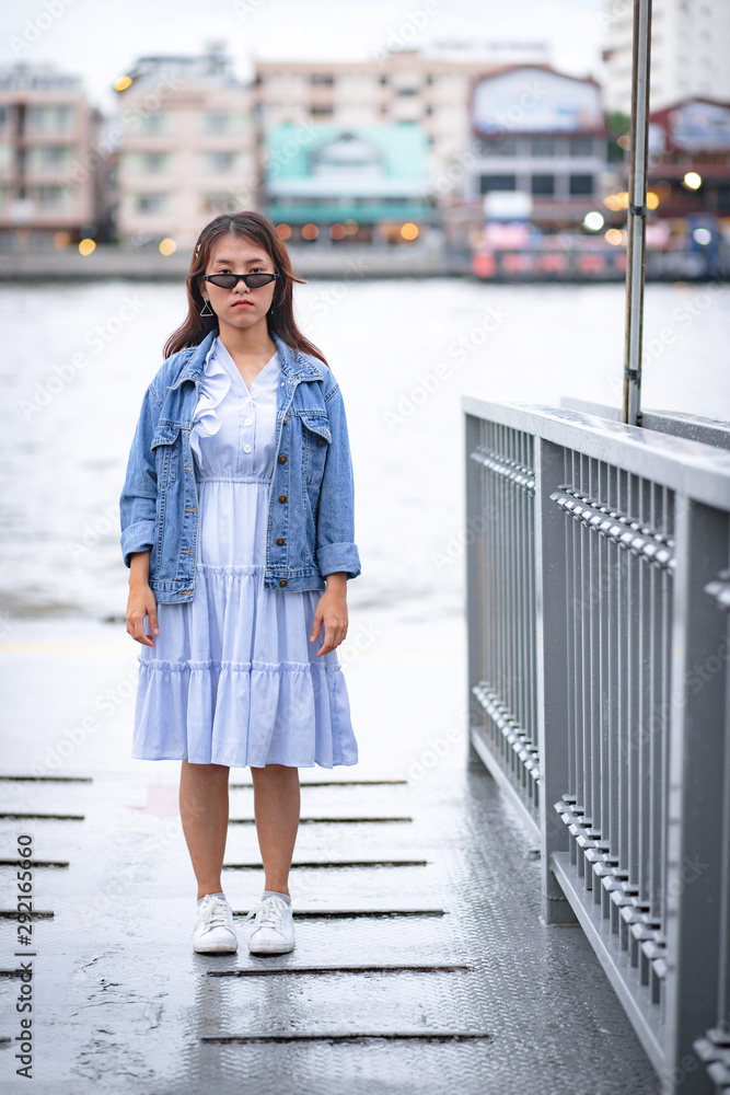Portrait of adorable Asian woman in blue dress, jean jacket and sunglasses