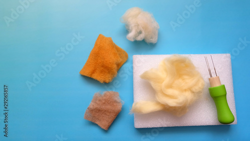 Flat lay of brown and beige felt wool and felting kit of felt needle and sponge.