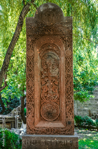 Old stone khachkar with figures of saints in a circle, framed by a carved weave of grape twigs, pomegranate and disks of the sun in the park of the Church 