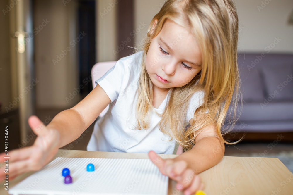 Little blonde girl in a white tshirt playing with plastic multicolor mosaic at home or preschool. Early education concept. Little blonde girl in a white tshirt playing with plastic multicolor mosaic at home or preschool. Early education concept.