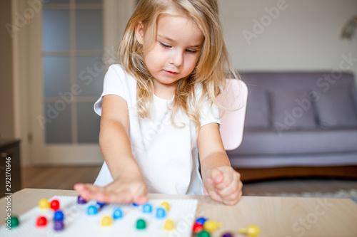 Little blonde girl in a white tshirt playing with plastic multicolor mosaic at home or preschool. Early education concept.