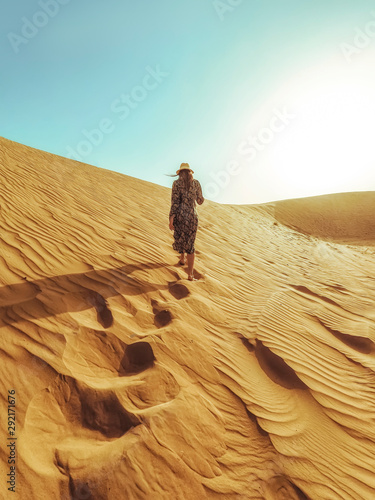 Young beautiful woman in a long dress walks along the sand dunes of the Dubai desert