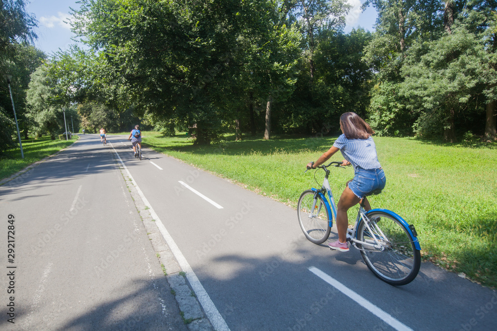 Pretty Young Woman Riding Bicycle In The Park Rear View