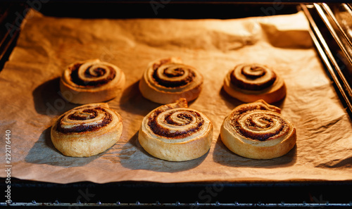 Sweet homemade vegan cinnamon rolls on baking paper in a lit up oven