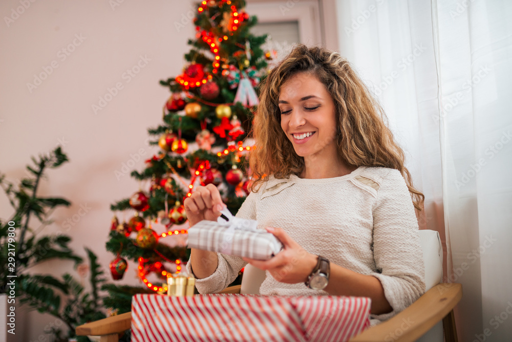 Portrait of a positive young woman opening present at Christmas time. Portrait of a positive young woman opening present at Christmas time.