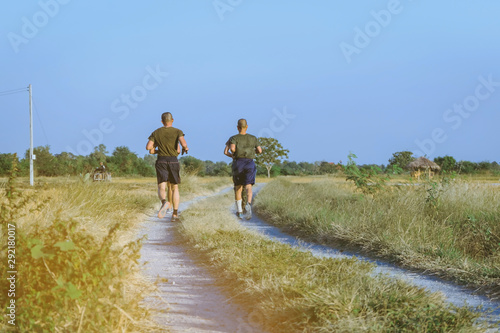 Back view of men running and exercising with friends together on the path through the rice fields in the evening.