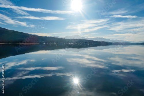 A view on a lake and Alps in the back. The calm surface of the lake is reflecting the mountains, sunbeams and clouds. Clear and sunny day. Calm and relaxed feeling. photo