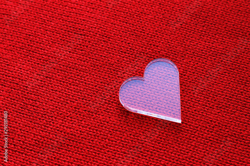 White transparent plastic toy heart on red knitted fabric. St. Valentine day  romantic card with copy space.