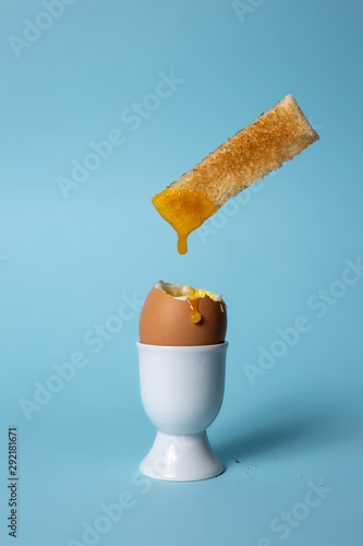 Bild auf Leinwand Soft boiled egg in egg cup on blue background with toast soldiers