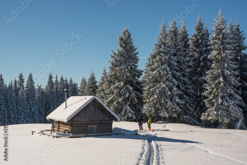 People near snow covered wood  hut. Frosted forest in background.