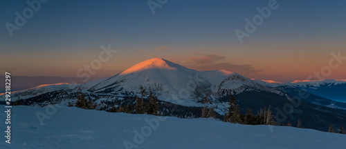 Winter morning in mountains. Illuminated mountain top in middle of composition.