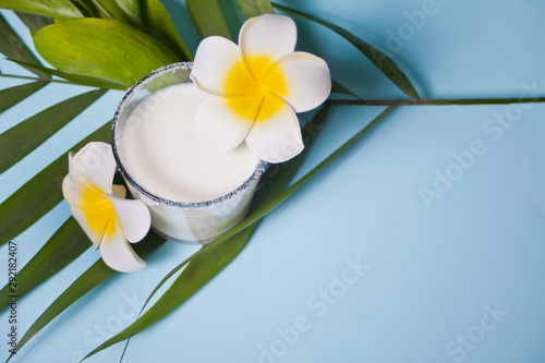 Glass of coconut milk with flowers plumeria and palm leaf, Top view. Copy space