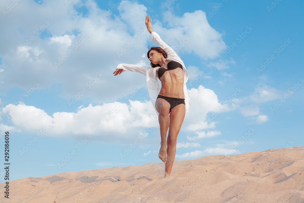 Obraz premium Happy healthy fit woman dancing on sand at the beach in her bikini, copy space. Stunning sexy female dancer performing in the desert. Health, femininity concept