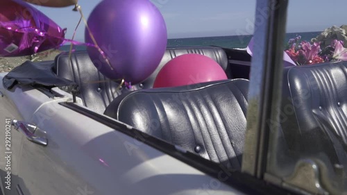 View of a classic open top vintage cabriolet car on the beach decorated by balloons for a celebration