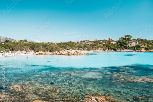 Beach with people enjoying in the crystal clear waters of Sardinia, Italy 