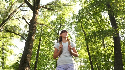 Hiker woman walks in the forest. Girl traveler is walking through the woods with backpack. happy hiker girl in summer park. teenager girl adventures on vacation.