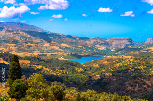 Scenic view of cretan landscape at sunset.Typical for the region olive groves, olive fields, vineyard and narrow roads up to the hills. Potami dam lake in foreground.
