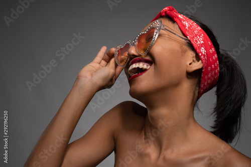 Portrait of smiling pretty Asian pinup girl with sunglasses isolated over gray wall background