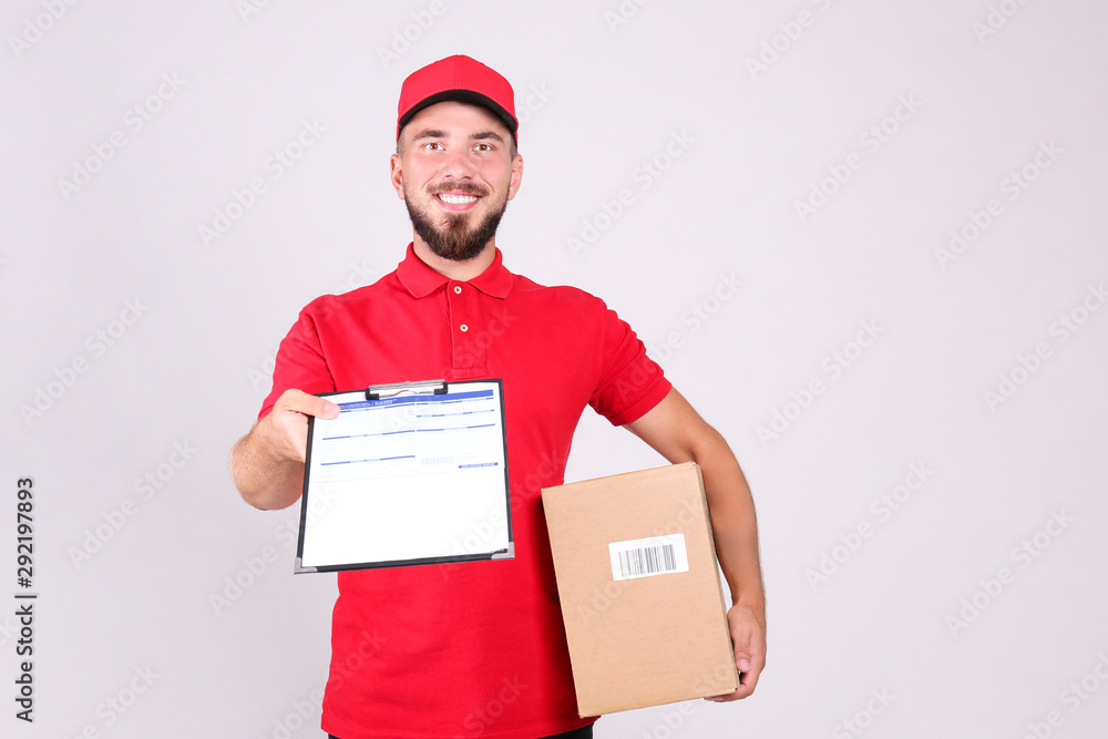 Young handsome delivery guy wearing red uniform and cap holding the blank cardboard box over isolated white background. Portrait of friendly bearded man carrying parcel. Copy space for text.
