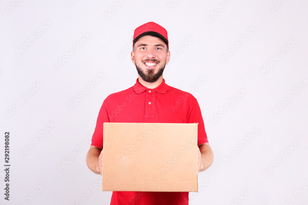 Young handsome delivery guy wearing red uniform and cap holding the blank cardboard box over isolated white background. Portrait of friendly bearded man carrying parcel. Copy space for text. Young handsome delivery guy wearing red uniform and cap holding the blank cardboard box over isolated white background. Portrait of friendly bearded man carrying parcel. Copy space for text.