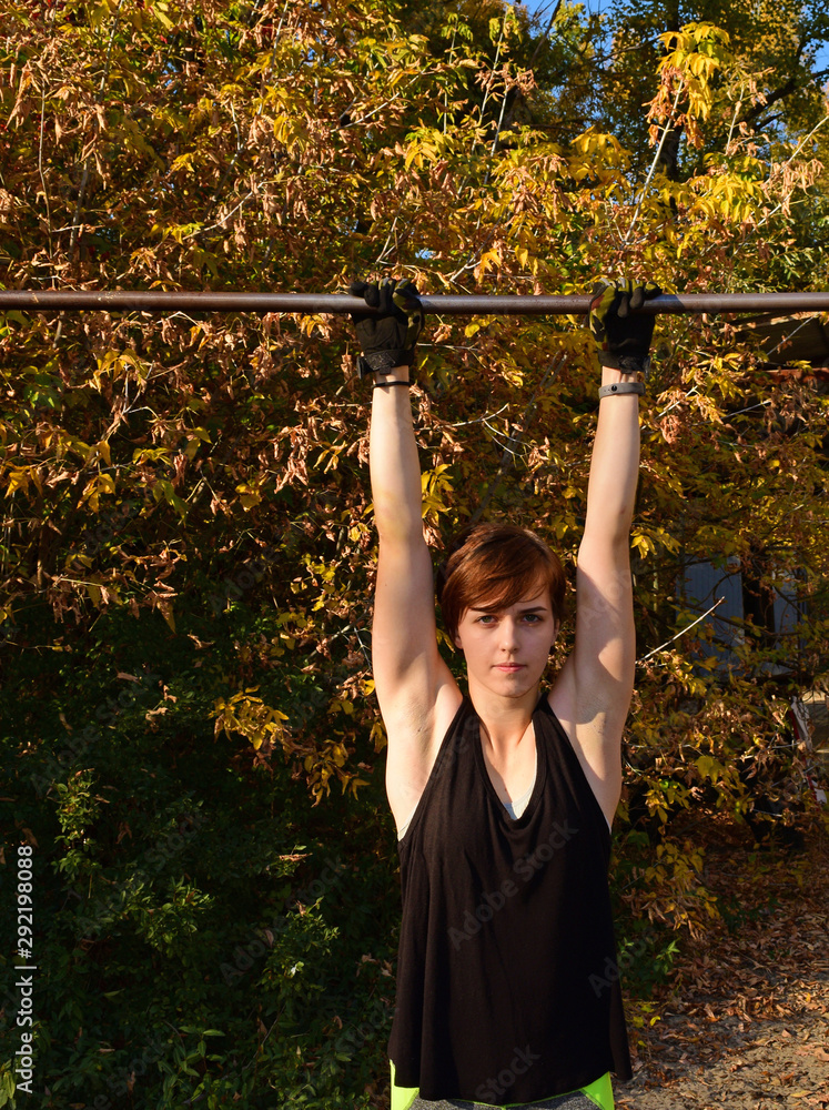 Young sporty girl hanging on a sports bar anf background of autumn foliage. Young sporty girl hanging on a sports bar anf background of autumn foliage.