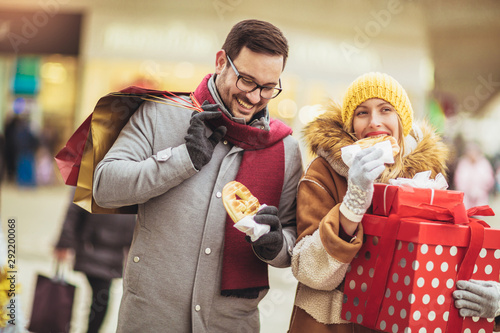 Young couple dressed in winter clothing holding gift boxes outdoor. They eat pretzels.Selective focus.