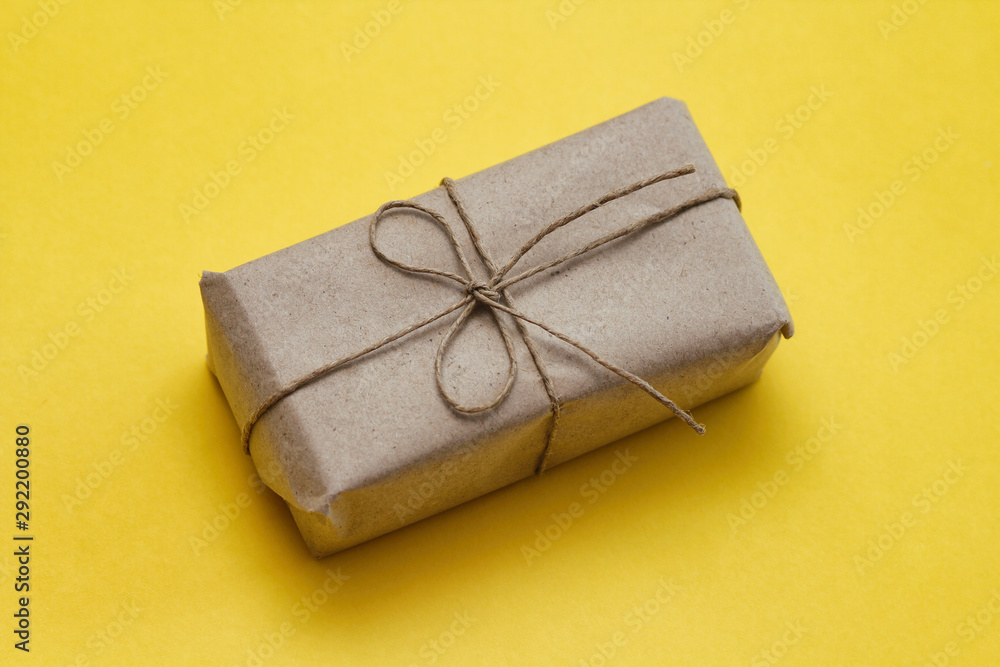 Parcel wrapping in brown craft paper and tie hemp string. Package. Delivery service. Online shopping. Your purchase. Gift box on a table. Yellow solid background. Parcel wrapping in brown craft paper and tie hemp string. Package. Delivery service. Online shopping. Your purchase. Gift box on a table. Yellow solid background.
