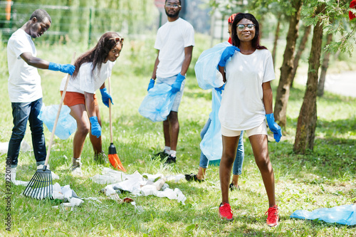 Group of happy african volunteers with garbage bags cleaning area in park. Africa volunteering, charity, people and ecology concept.